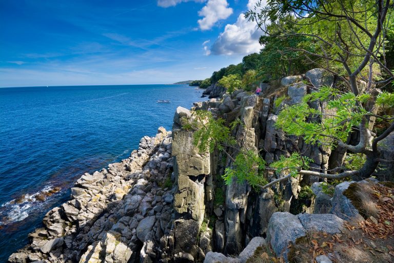 Sheer cliffs of the northern coast of Bornholm island - Helligdomsklipperne (Sanctuary Rocks), Gudhjem town in the background, Denmark